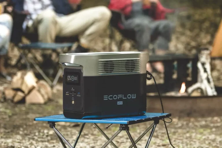 EcoFlow Delta Mini-8 tragbare Powerstation auf einem Tisch im Freien, umgeben von Campingstühlen und einem Lagerfeuer.