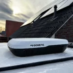 Dometic Breathe 3100 Belüftungssystem auf einem Fahrzeugdach, mit sichtbaren Wassertropfen und Solarpanelen im Hintergrund.